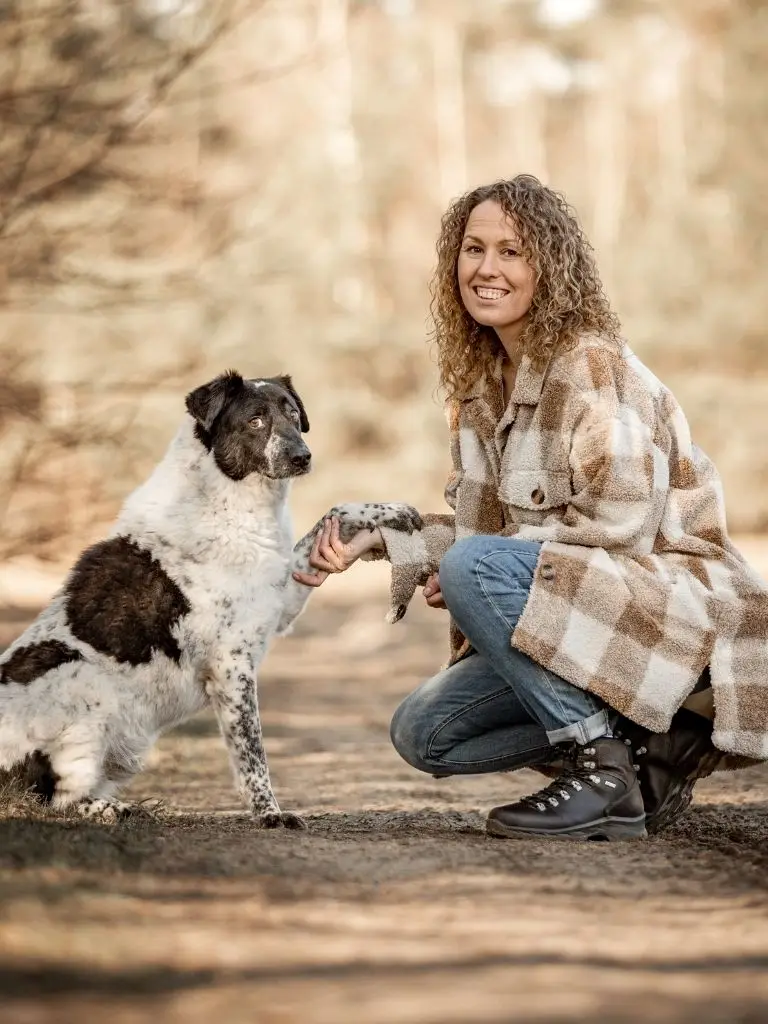 Sandra von der Hundeschule Klippo kniet auf dem Boden hält die Pfote eines Hundes in der Hand, beide schauen in die Kamera