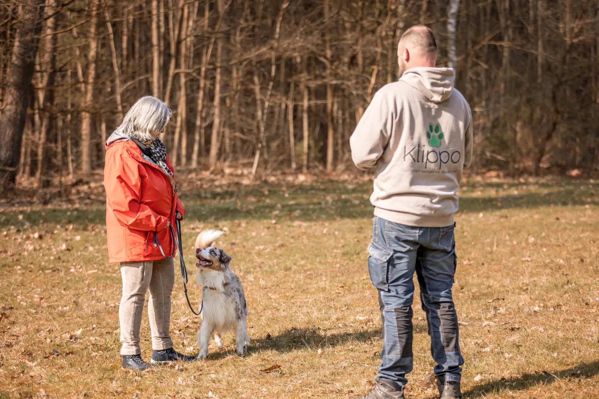 Eine Hundebesitzerin steht neben ihrem Hund. Er schaut sie vertraut an. Vor ihnen steht Meik Gauda, Hundetrainer der Klippo Hundeschule